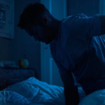 Man in a bedroom at night holding his lower back in discomfort, illustrating possible kidney stone symptoms