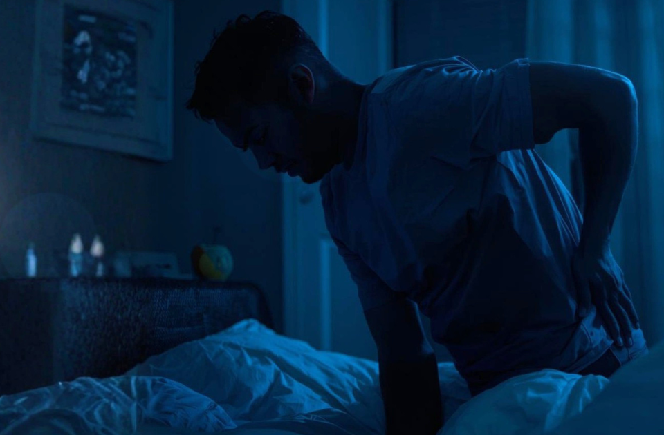 Man in a bedroom at night holding his lower back in discomfort, illustrating possible kidney stone symptoms